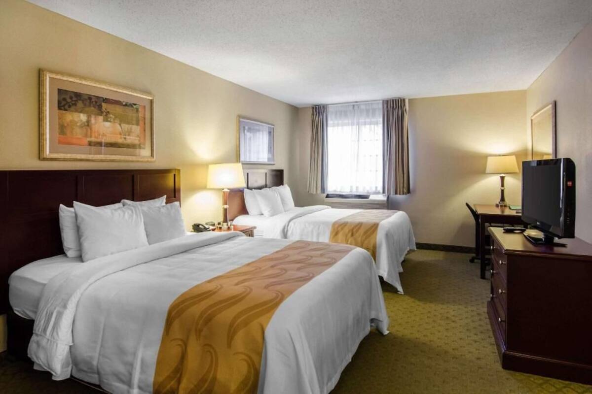 A hotel room with two beds, a desk, a TV, and a painting on the wall.