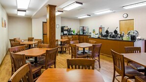 A dining area with wooden tables and chairs, a counter with kitchen appliances, and a clock on the wall.