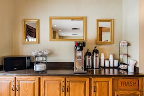 A hotel kitchenette with a microwave, coffee maker, and coffee cups.