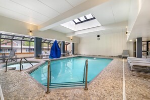 An indoor swimming pool with a tiled floor, a skylight, and a clock on the wall.