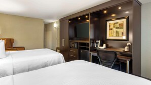A hotel room with two beds, a desk, a chair, a television, and a small refrigerator.