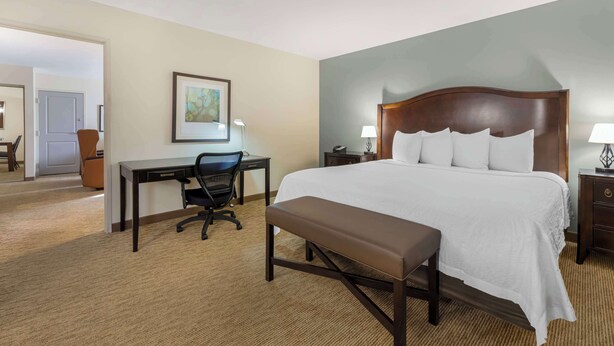 A hotel room with a large bed, a desk, a chair, and a bench.