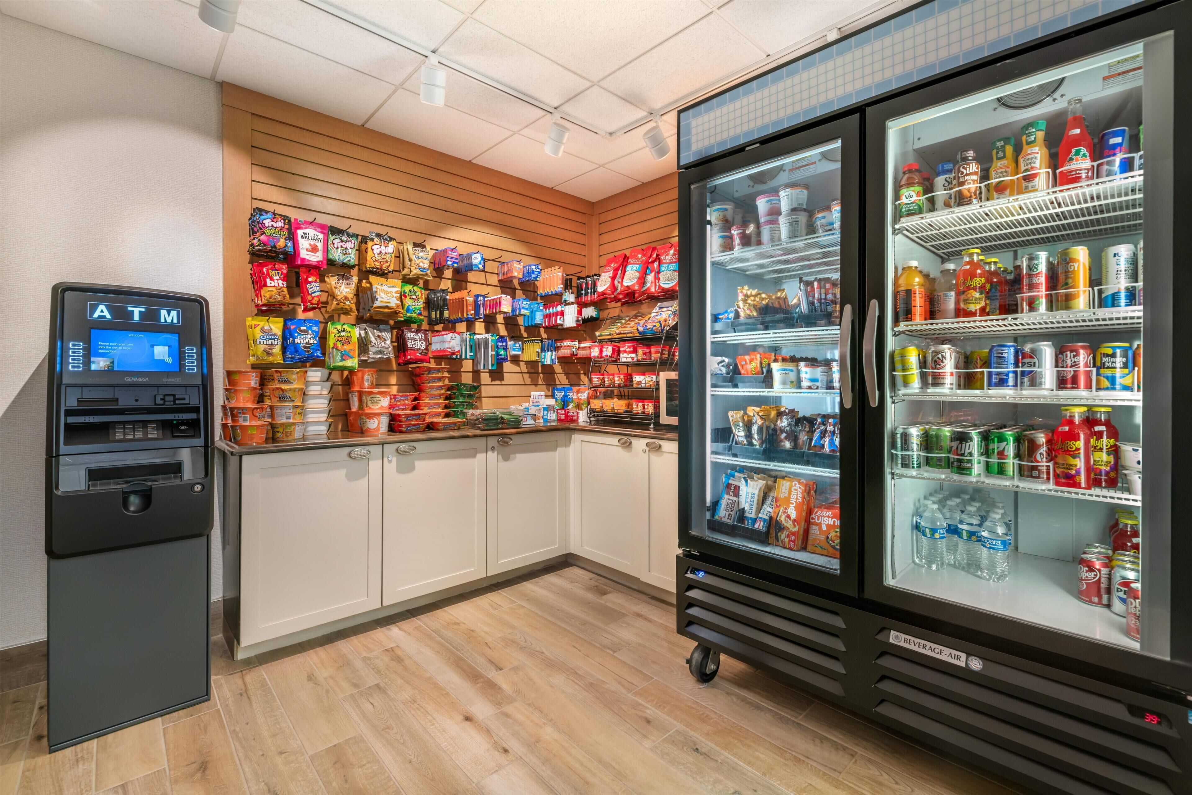 Un distributeur automatique de billets, des étagères de snacks et un réfrigérateur à boissons dans un magasin.