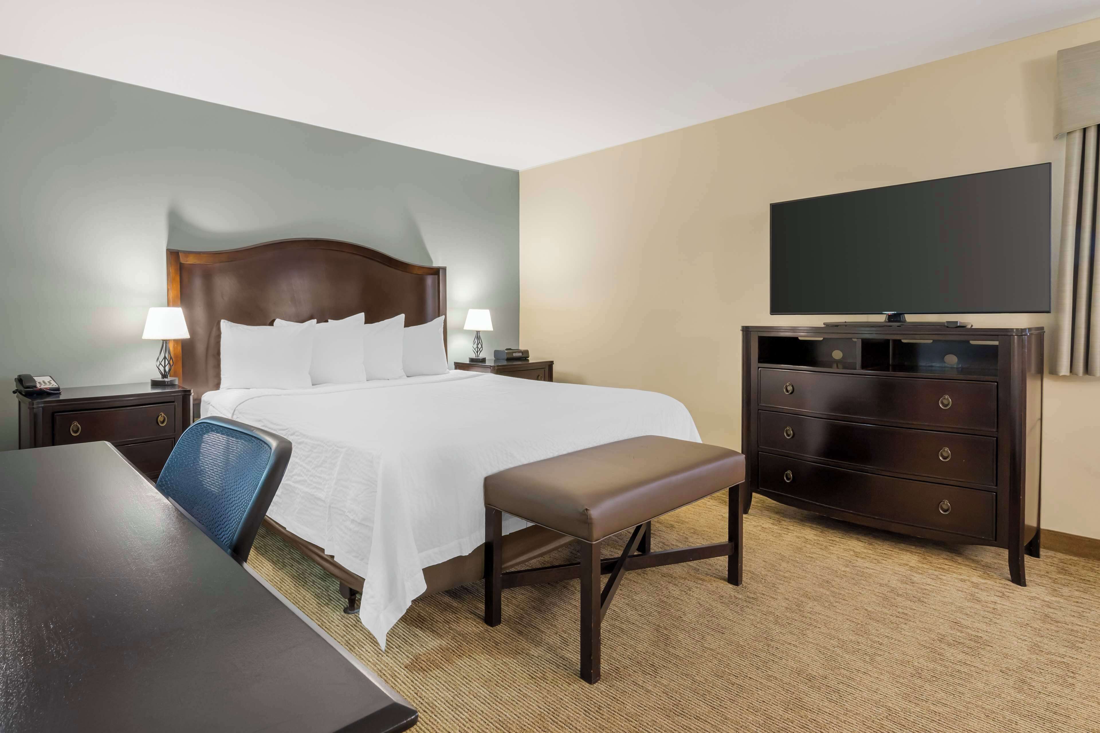 Een hotelkamer met een bed, een bureau, een stoel, een dressoir en een televisie.