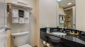 Un baño con inodoro, lavamanos, espejo y toallero con toallas.