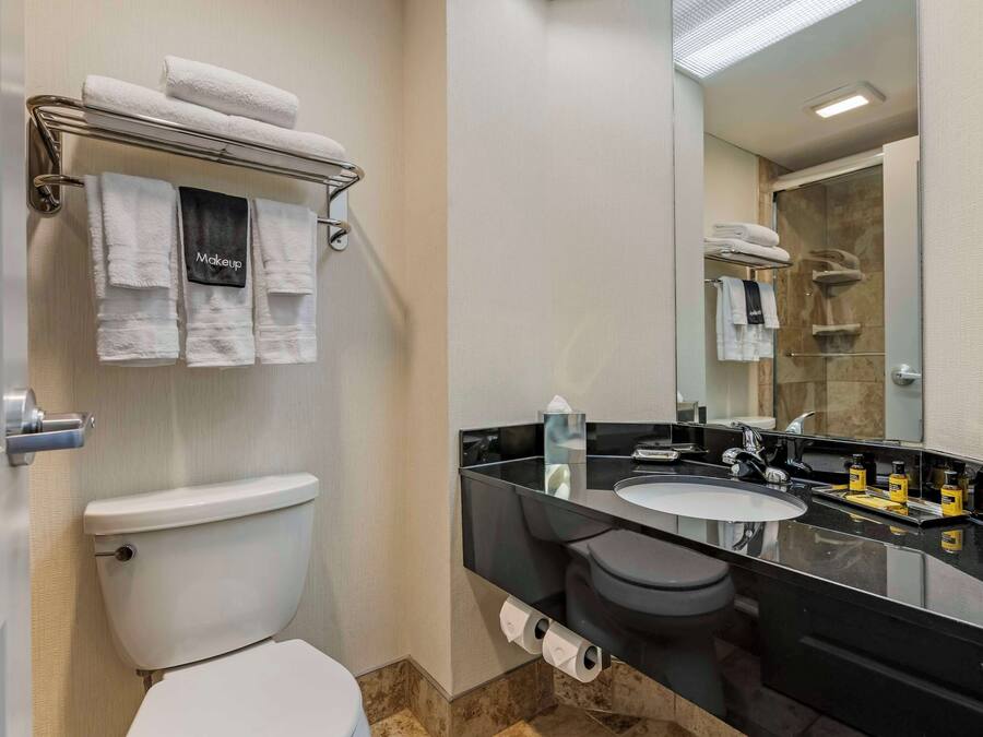 Un baño con inodoro, lavamanos, espejo y toallero con toallas.
