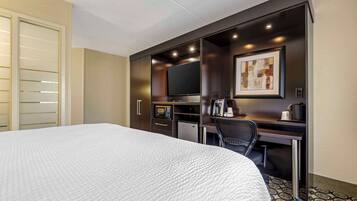 Habitación de hotel con una cama grande, un escritorio con televisor de pantalla plana, un refrigerador pequeño, un microondas y una cafetera.
