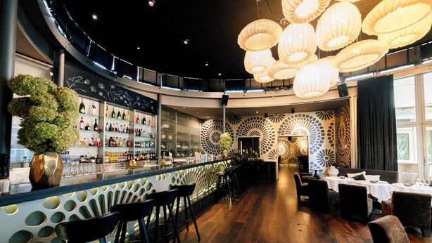 A bar area with a curved counter, multiple seating options, and a decorative wall with circular patterns. - Park Hotel Winterthur (Winterthur)
