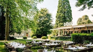 An outdoor dining area with tables and chairs, surrounded by greenery and trees. - Park Hotel Winterthur (Winterthur)