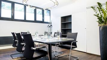 A modern meeting room with a round table, black chairs, and a large potted plant.