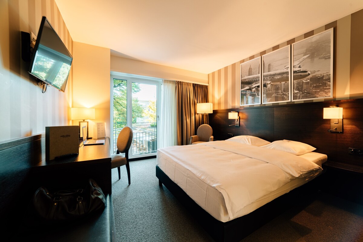 A hotel room with a bed, desk, chair, TV, and a view of the outdoors.