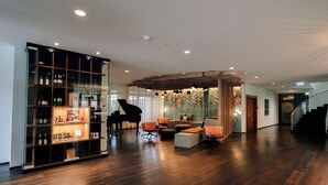 A spacious living area with a grand piano, seating arrangements, and a wine display. - Park Hotel Winterthur (Winterthur)