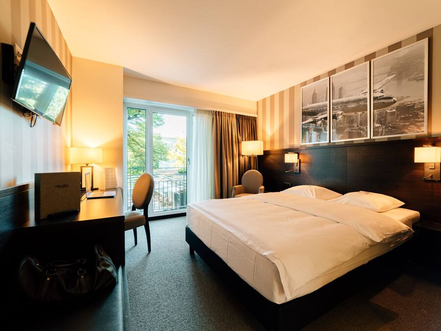 A hotel room with a bed, desk, chair, TV, and a view of the outdoors.