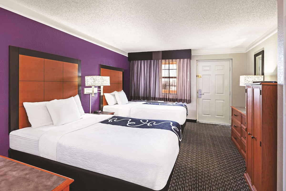 A hotel room with two beds, a dresser, a desk, and a window with curtains.