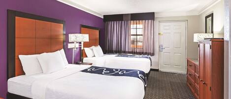 A hotel room with two beds, a dresser, a desk, and a window with curtains.
