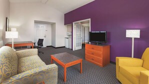 A hotel room with a sofa, a small table, a TV on a wooden stand, and a yellow armchair. - La Quinta Inn by Wyndham Midland (Midland)