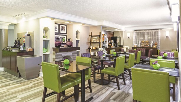 A modern dining area with green upholstered chairs, a glass-top table, and a kitchen area with a built-in stove and various kitchen appliances. - La Quinta Inn by Wyndham Midland (Midland)