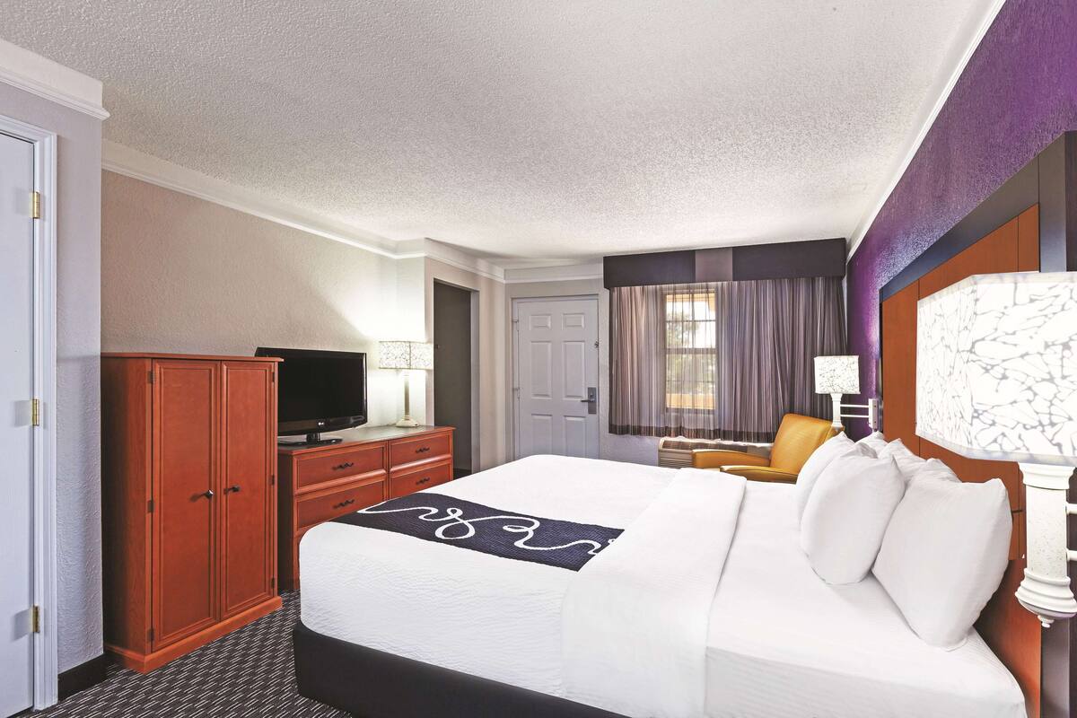 A hotel room with a large bed, a wardrobe, a television, and a desk with a chair.