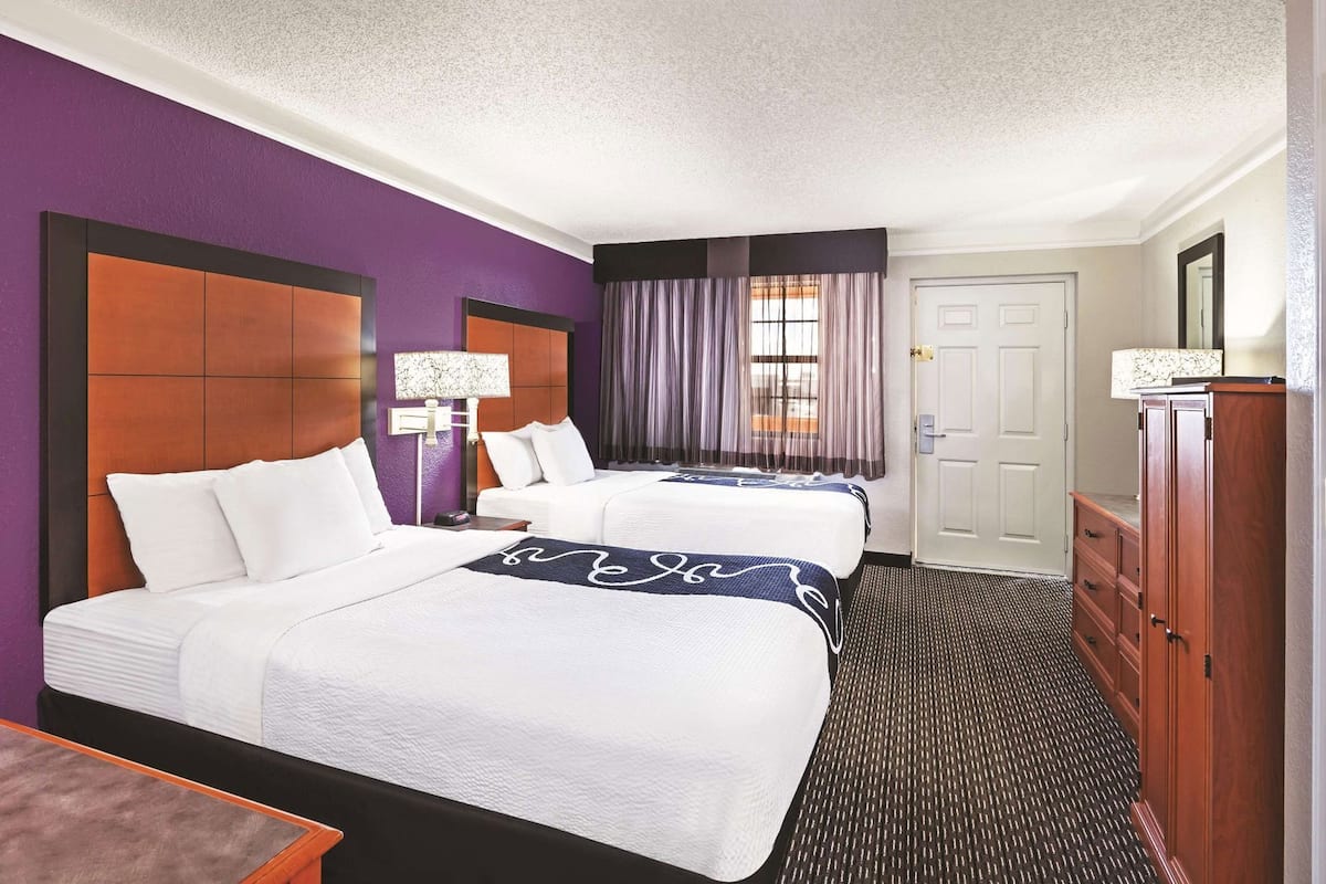 A hotel room with two beds, a dresser, a lamp, and a window with curtains.