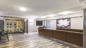 A reception area with a wooden reception desk, a large floral wall decoration, and a patterned floor. - La Quinta Inn by Wyndham Midland (Midland)
