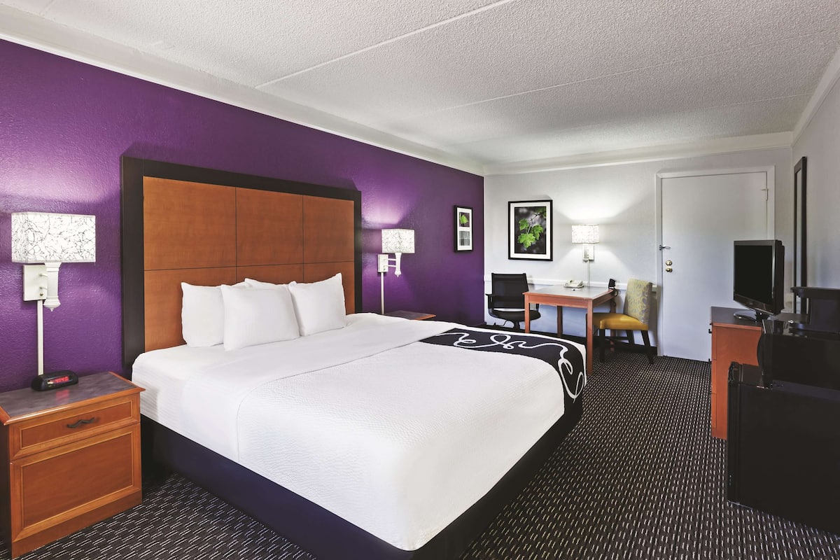 A hotel room with a large bed, a desk, a chair, a television, and a door.
