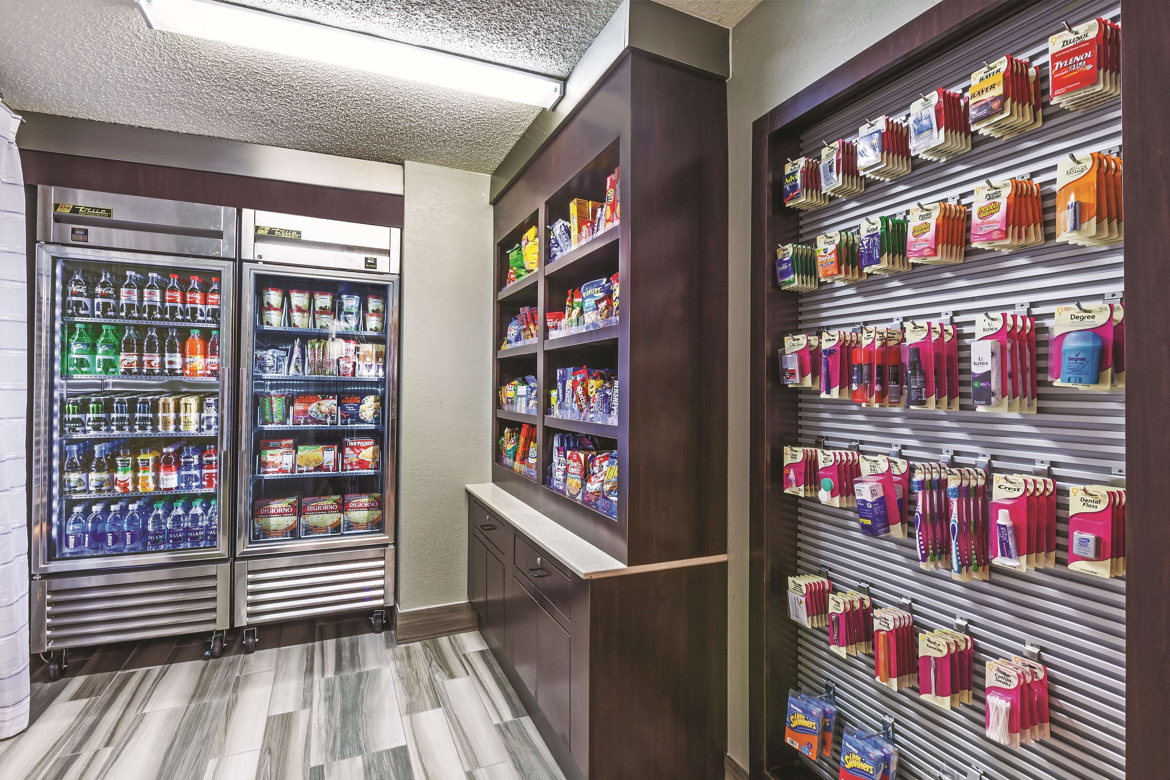 Et hotel lobby med to drikkemaskiner, en snackbar og et stativ med toiletartikler.