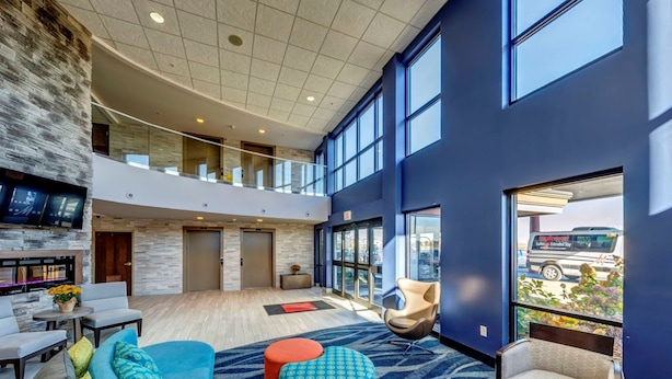 A spacious lobby with a high ceiling, a stone accent wall, and a large window offering a view of the outside.