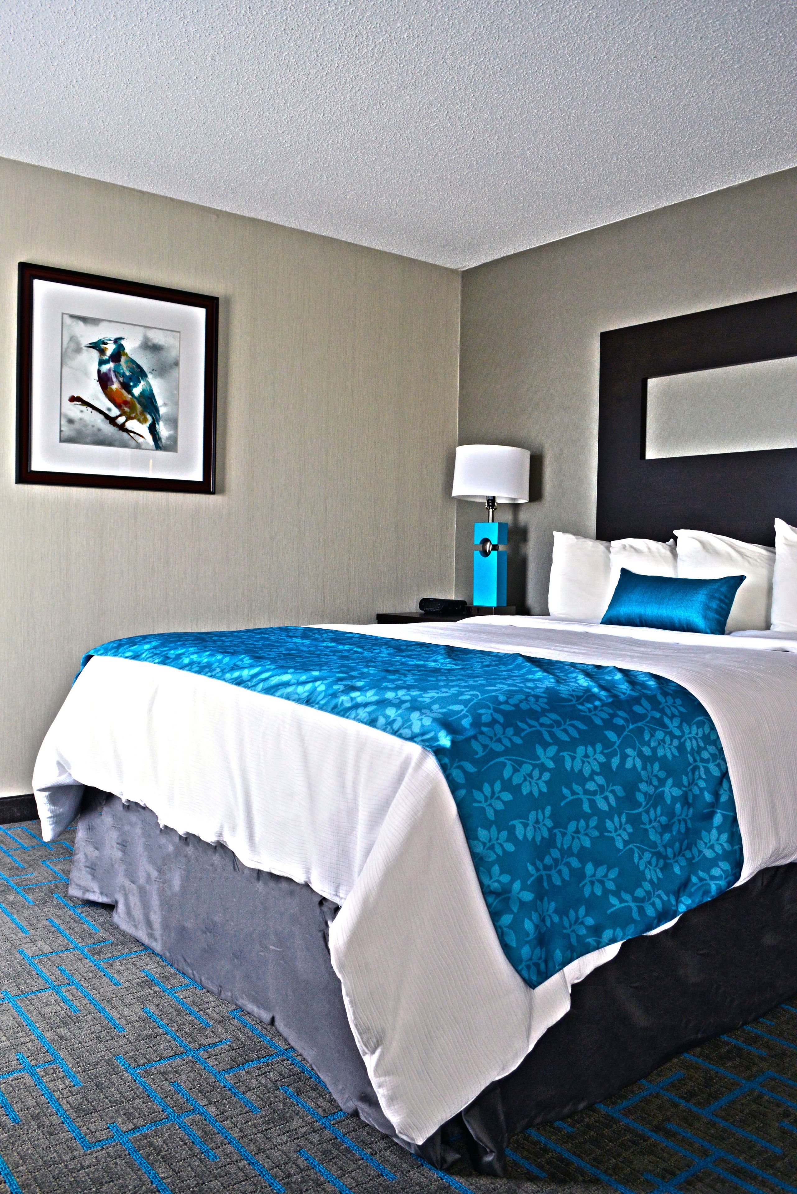 A hotel room with a large bed, a nightstand, a lamp, and a framed picture on the wall.