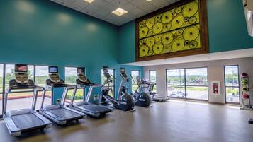 A gym with treadmills, ellipticals, and a large window with a view of a parking lot.