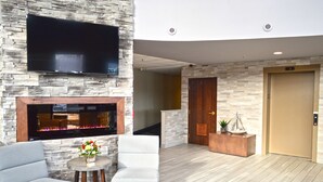 A lobby with a stone wall, a flat-screen TV, a fireplace, seating, and an elevator.
