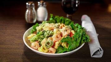 Un bol de salade de pâtes aux crevettes, avec une serviette en papier et des salières et poivrières sur une table en bois.
