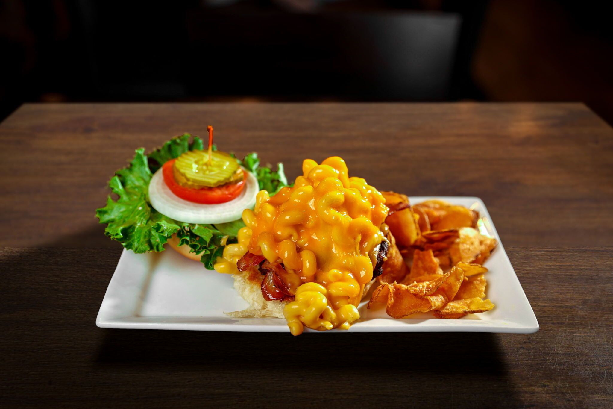 A plate of macaroni and cheese with bacon, a slice of tomato, and lettuce on a white plate.