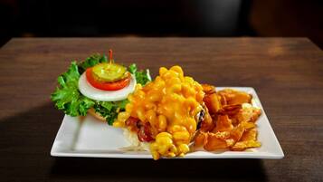 A plate of macaroni and cheese with bacon, a slice of tomato, and lettuce on a white plate.