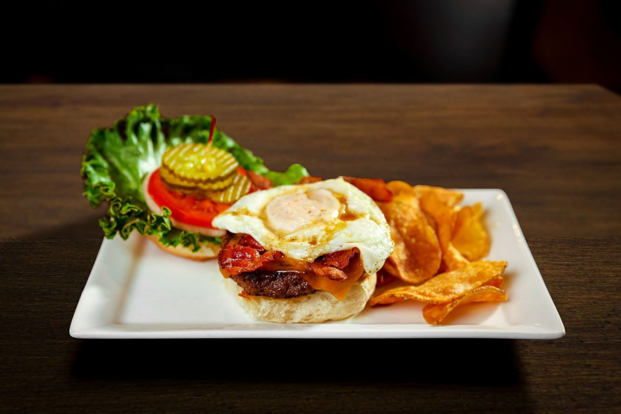 A plate with a sandwich, a fried egg, and potato chips.