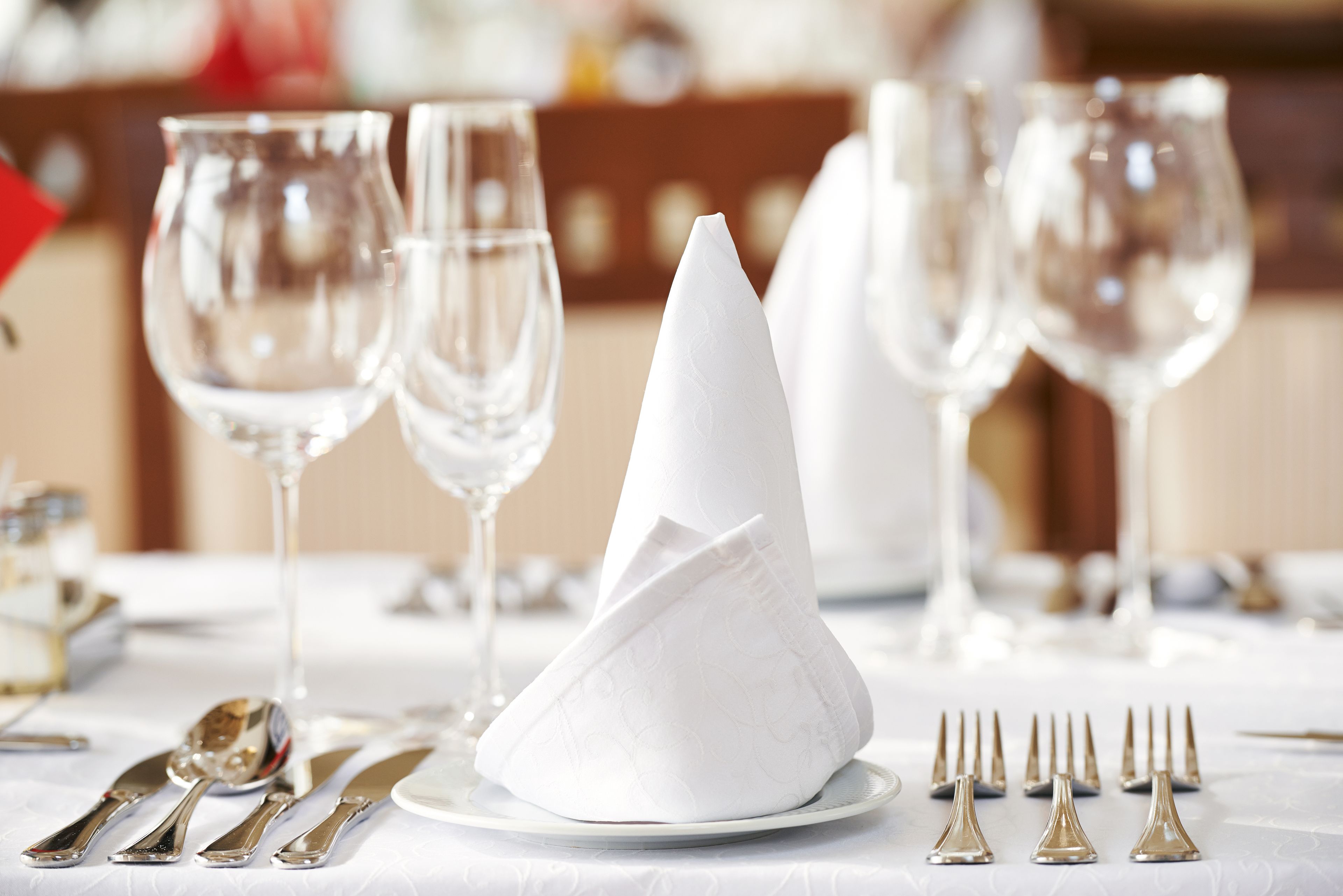 Une table dressée avec des serviettes blanches, des couverts en argent et des verres à vin transparents.