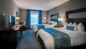 A hotel room with two beds, a desk, a chair, a lamp, and a window with curtains.