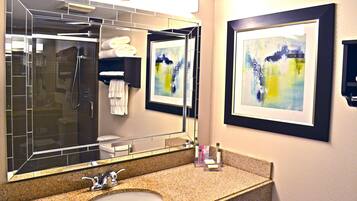 A bathroom with a large mirror, a sink, a shower, and two framed abstract paintings on the wall.