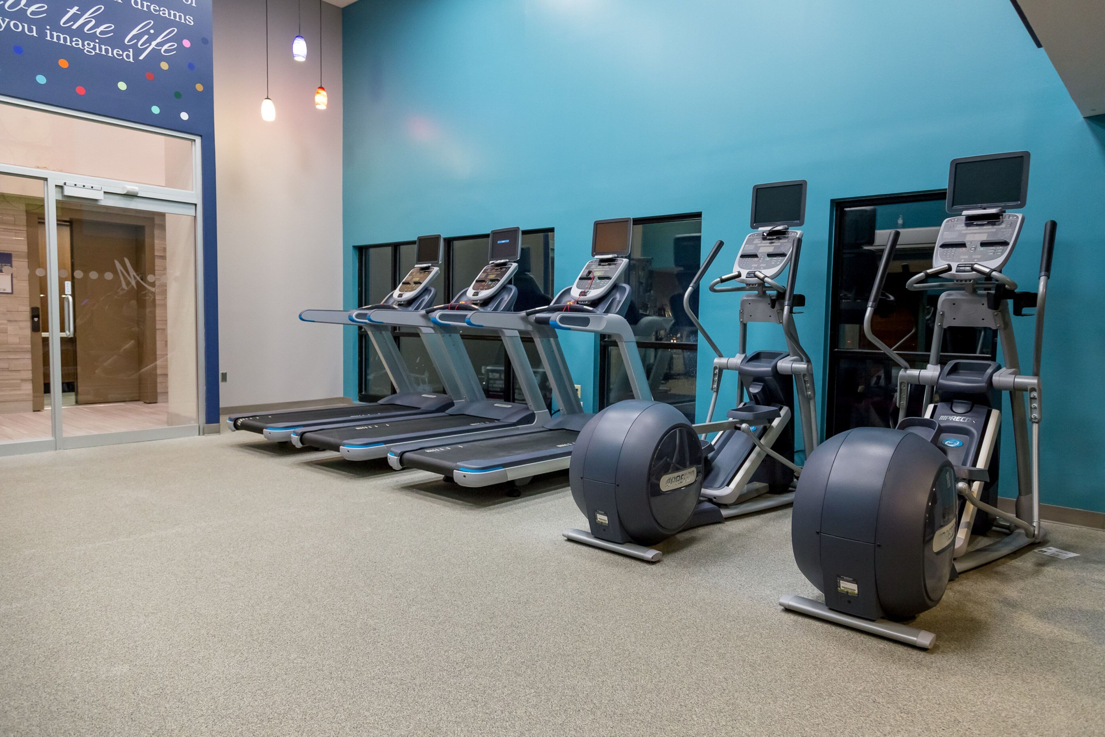Un gimnasio con cintas de correr, elípticas y una bicicleta estática.