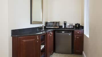 Uma cozinha compacta com armários de madeira escura, bancada preta, micro-ondas embutido, cafeteira e máquina de lavar louça.