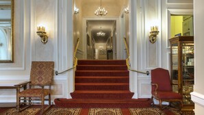 A grand staircase with a red carpet, flanked by two ornate chairs and a chandelier. - Beresford Arms Hotel (San Francisco)
