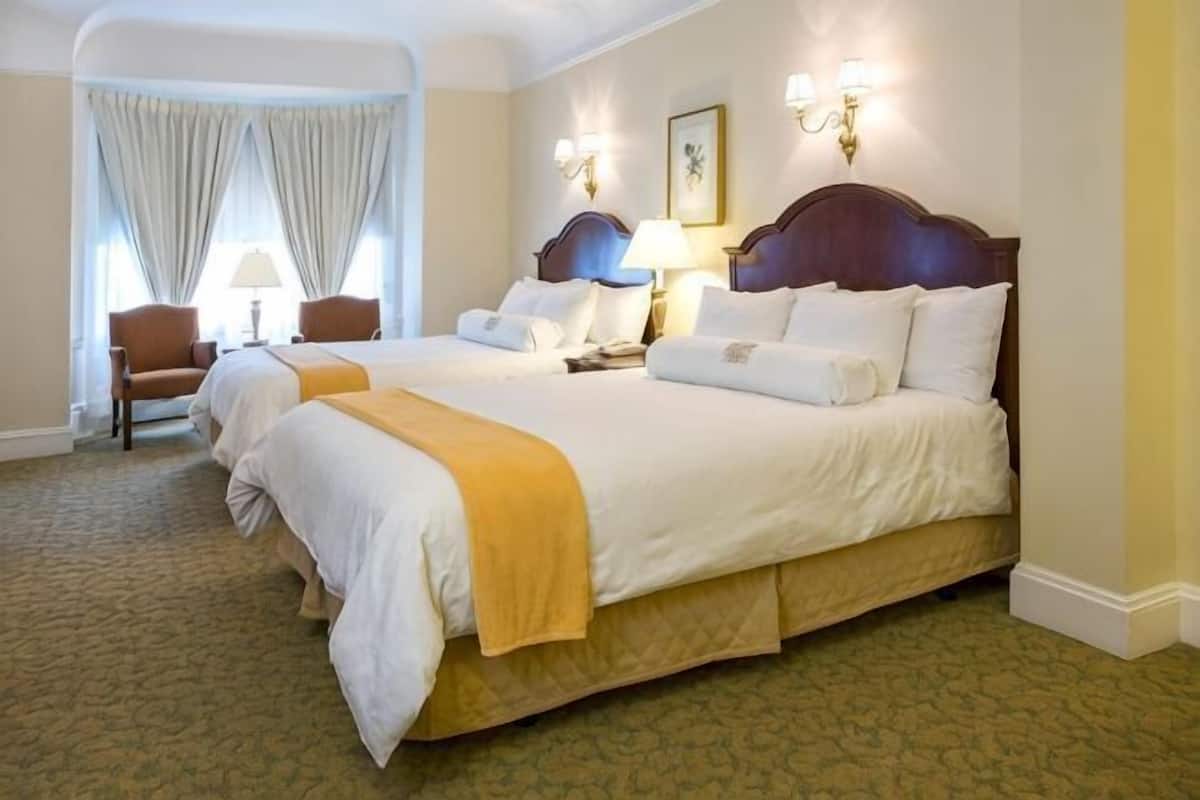 Ein Hotelzimmer mit zwei Betten, einem Sessel, einer Lampe und einem Gemälde an der Wand.