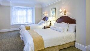 A hotel room with two beds, a window with sheer curtains, a bedside table with a lamp, and a painting on the wall. - Beresford Arms Hotel (San Francisco)