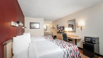 A hotel room with a bed, a desk, a chair, a TV, and a minibar.