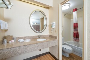 Un baño con encimera de granito, lavabo, espejo, secador de pelo y cortina de ducha.