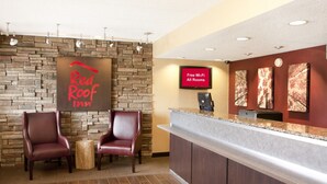 A Red Roof Inn reception area with a stone wall backdrop, two leather chairs, a wooden side table, and a digital display indicating free Wi-Fi availability. - Red Roof Inn Chesapeake Conference Center (Chesapeake)