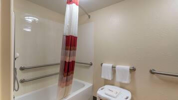 A bathroom with a bathtub, a shower curtain, a towel rack, and a small stool.
