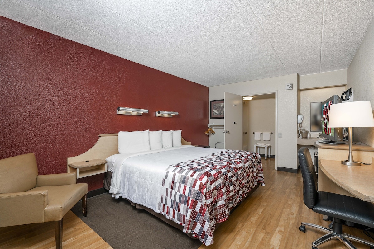A hotel room with a large bed, a desk, a chair, a small table, and a mirror.