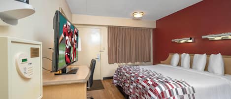 A hotel room with a bed, a desk with a computer, a television, and a control panel.