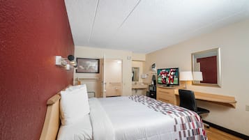 A hotel room with a bed, a desk, a television, and a bathroom door.