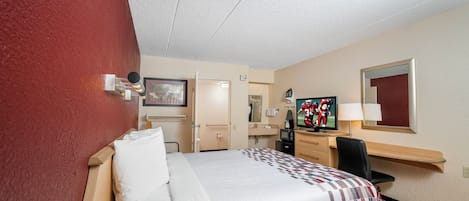 A hotel room with a bed, a desk, a television, and a bathroom door.